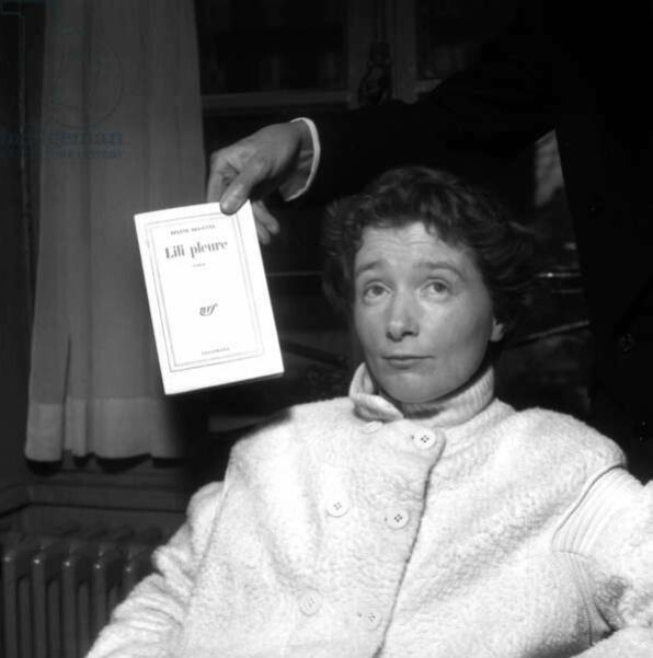 A seated Hélène Bessette with her book Lili pleure held next to her.