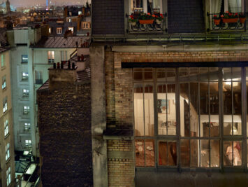 Nighttime view of a lit apartment window on rue de Douai in Paris. It looks in on a domestic scene and a woman reclining.