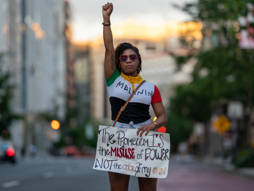 A Black woman raises her fist at a protest against police violence. Joyce by Miki J / Creative Commons
