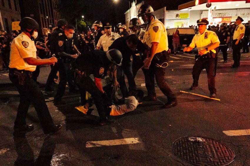 A group of police officers surround a man laying on the street