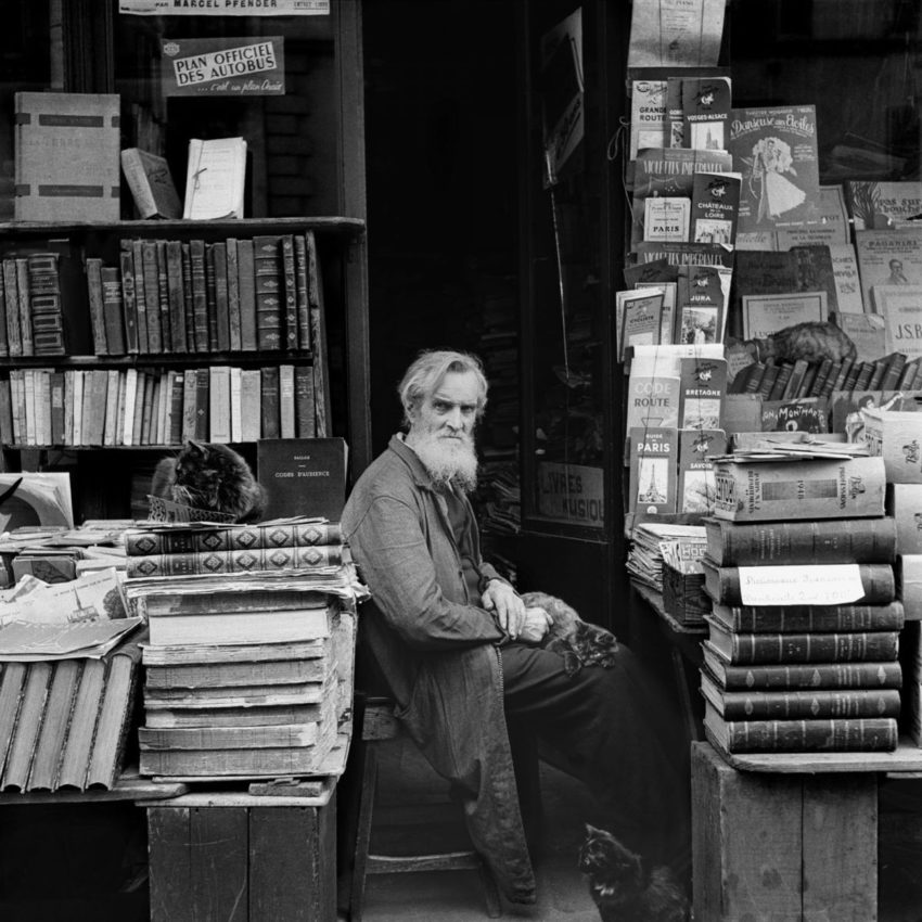 photo of man sitting amidst stacks and shelves of books