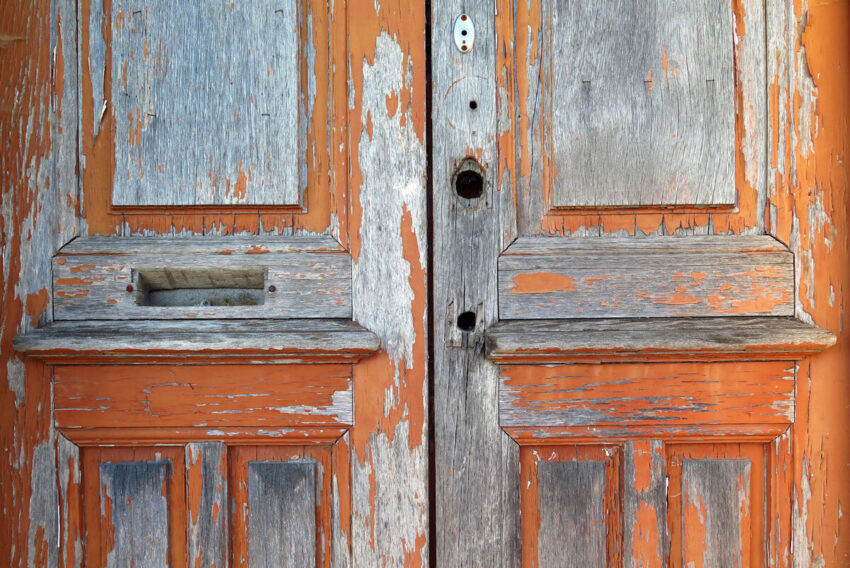 A pair of weathered wood doors with peeling orange paint