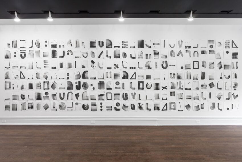 Installation of many peices of paper, each with black and gray shapes drawn on them.