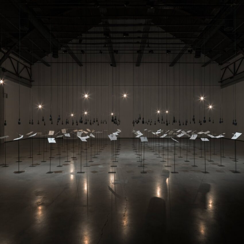 Installation view of many pieces of paper stuck on metal stands.