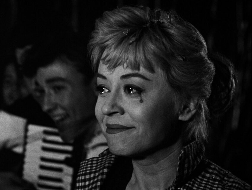 Black and white still showing Giulietta Masina smiling with a black tear at the corner of her eye